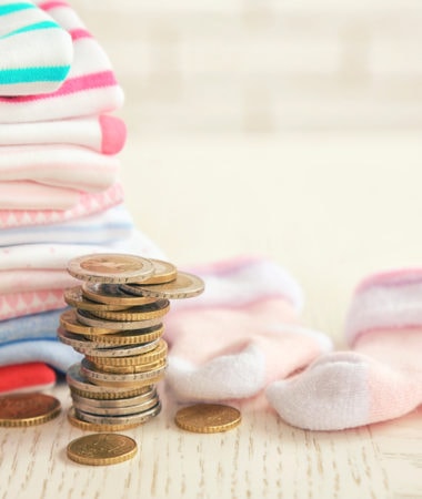 Parenting expenses concept. Pile of baby clothes and coins